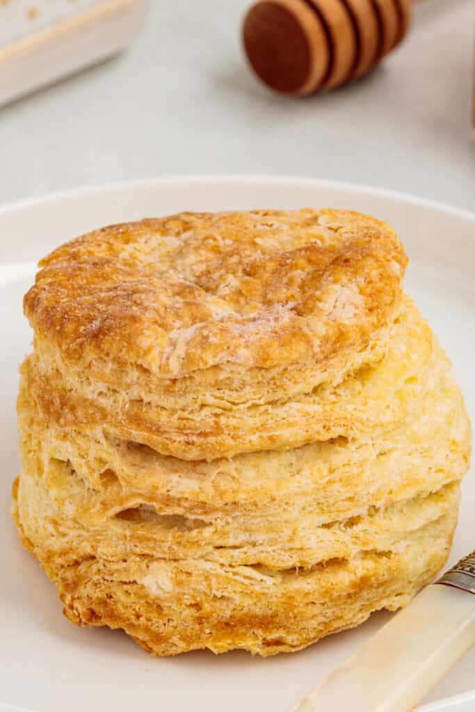 Close-up of a tall golden brown air fryer sour cream biscuit with visible flaky layers on a white plate.