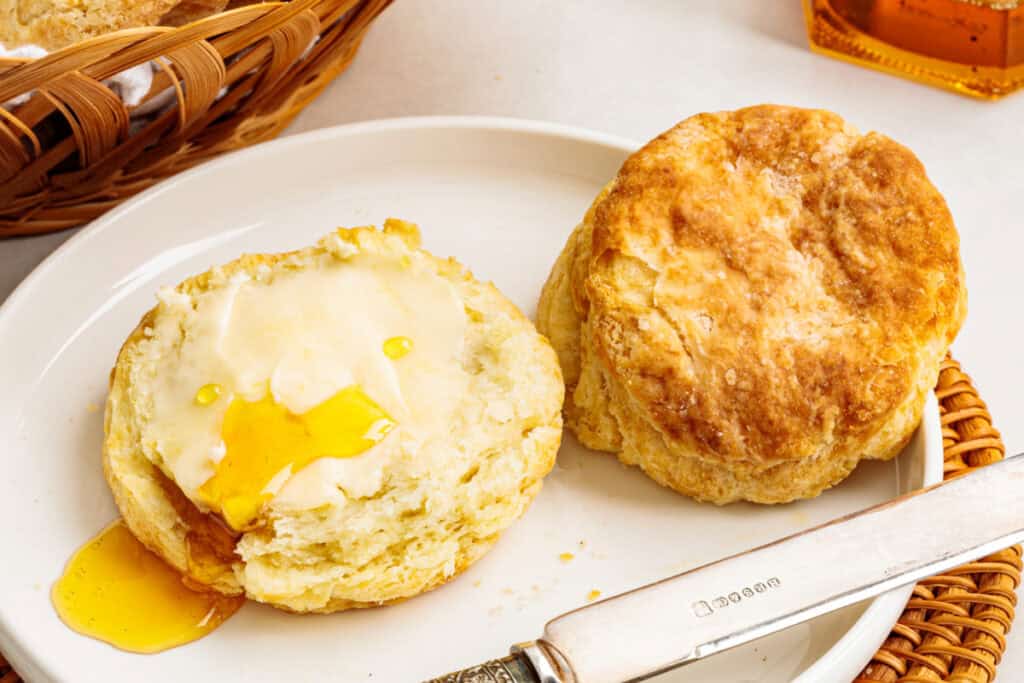 Air fryer sour cream biscuits served on a white plate, with one split and topped with butter and honey.
