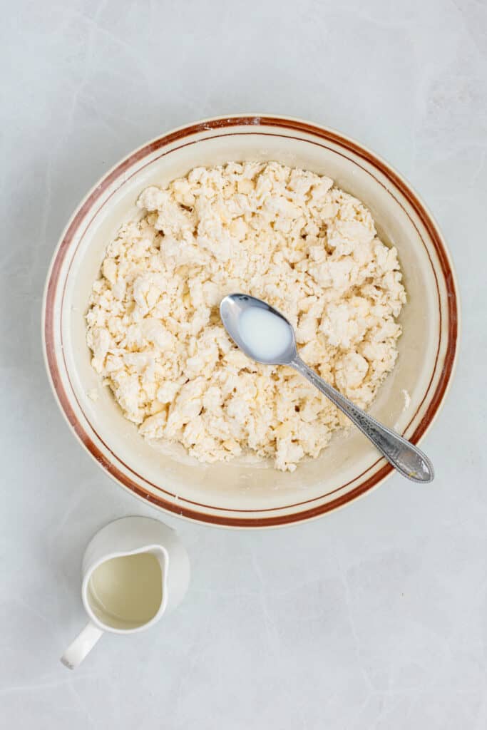 Shaggy sour cream biscuit dough coming together in a mixing bowl.
