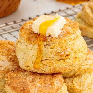 Close-up of a flaky air fryer sour cream biscuit topped with butter and honey, surrounded by golden biscuits.