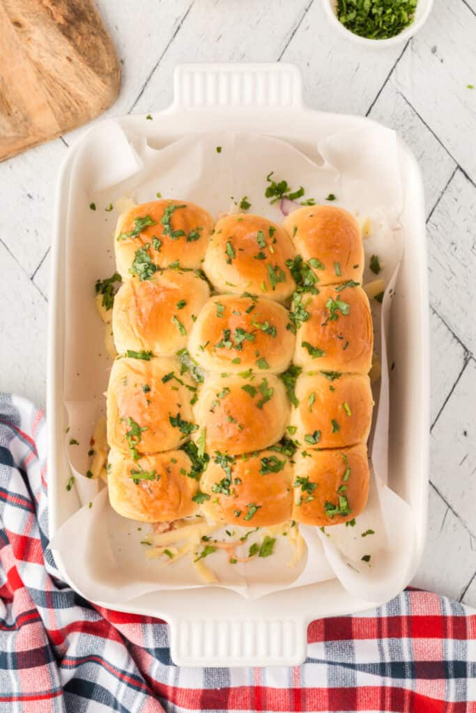Buttery slider buns topped with chopped cilantro and ready to be covered and baked.
