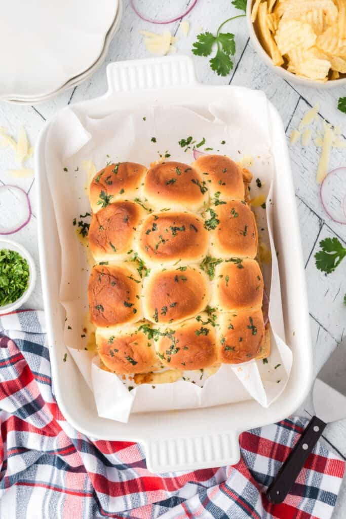 Freshly baked BBQ pulled chicken sliders with golden buns and cilantro in a baking dish.