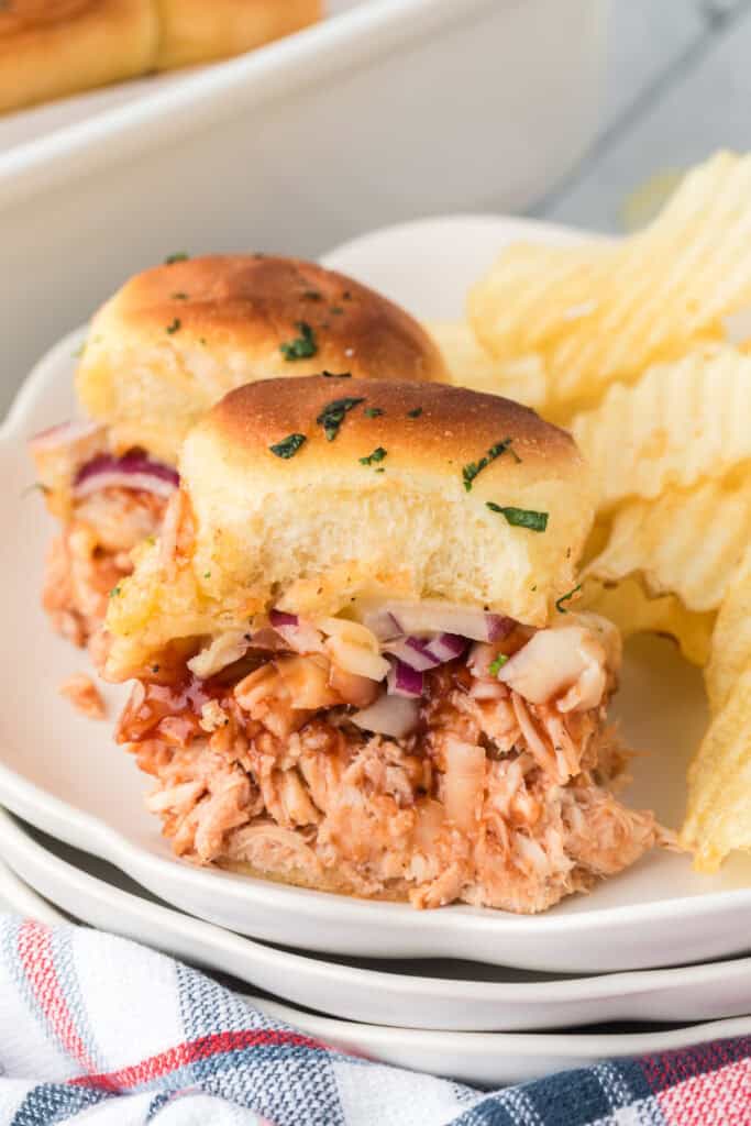 BBQ pulled chicken slider served with potato chips, showing saucy chicken, melted cheese, and red onion.