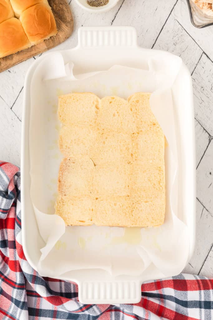 Bottom halves of slider buns arranged in a parchment-lined baking dish.