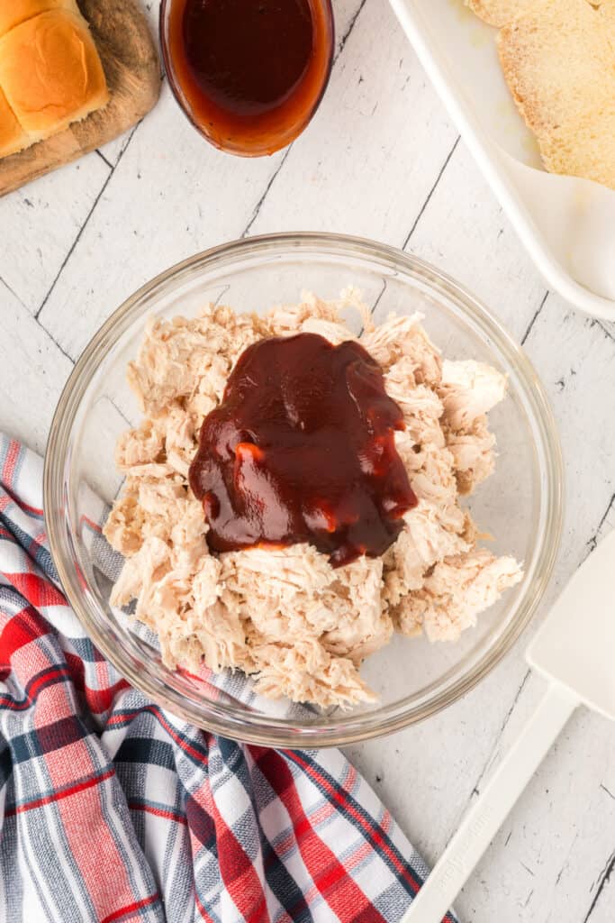 Shredded cooked chicken topped with BBQ sauce in a glass mixing bowl.
