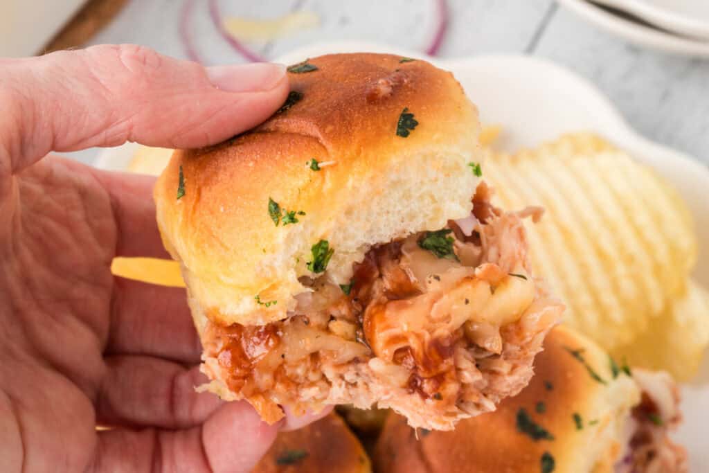 Close-up of a BBQ pulled chicken slider filled with shredded chicken, BBQ sauce, melted cheese, and red onion.