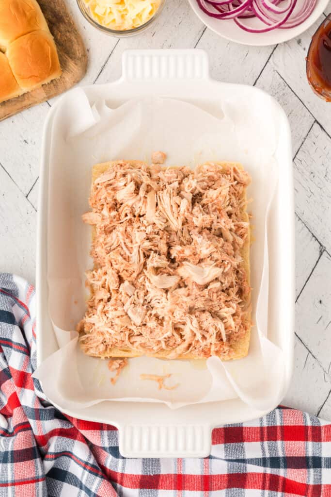 BBQ shredded chicken spread evenly over the bottom halves of the slider buns.