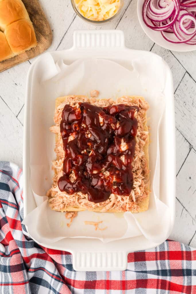 BBQ sauce spooned over shredded chicken while assembling BBQ chicken sliders.
