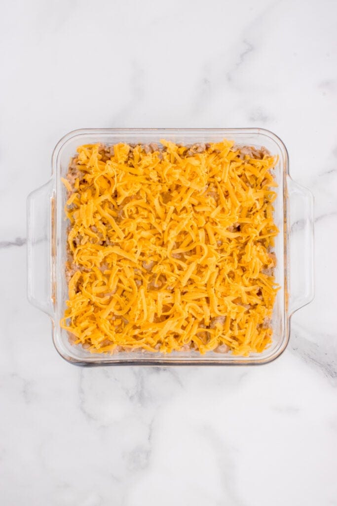 Shredded cheddar cheese layered over the ground beef mixture in a casserole dish.