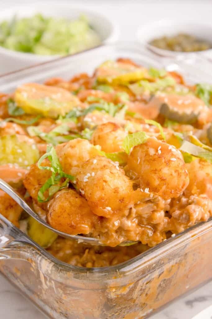 Spoonful of Big Mac Tater Tot Casserole with crispy tater tots, creamy ground beef, lettuce, pickles, dressing, and sesame seeds.