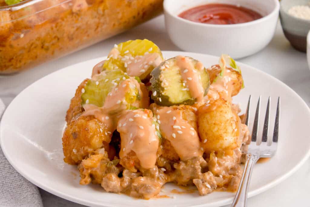 Big Mac Tater Tot Casserole served on a white plate with golden tater tots, pickles, burger sauce, and sesame seeds.