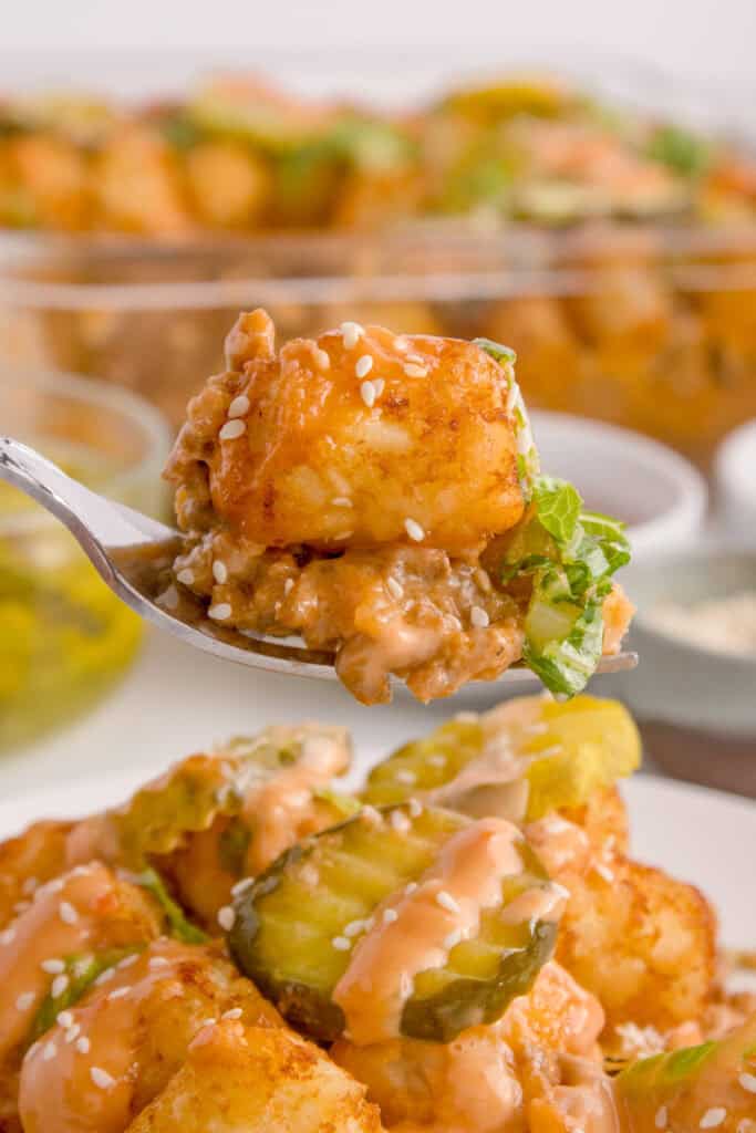 Close-up of a bite of Big Mac Tater Tot Casserole on a fork with a crispy tater tot, creamy beef filling, lettuce, and sesame seeds.