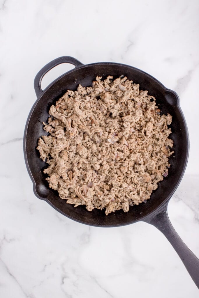 Cooked ground beef and onion in a cast-iron skillet for Big Mac Tater Tot Casserole.