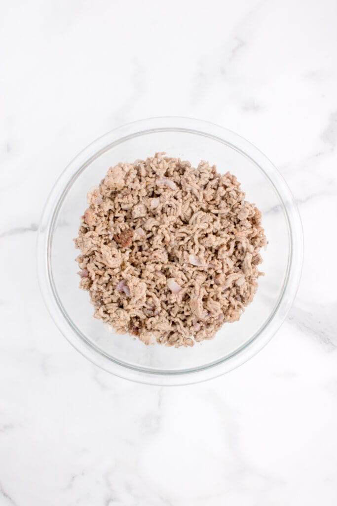 Cooked seasoned ground beef and onion transferred to a glass mixing bowl.