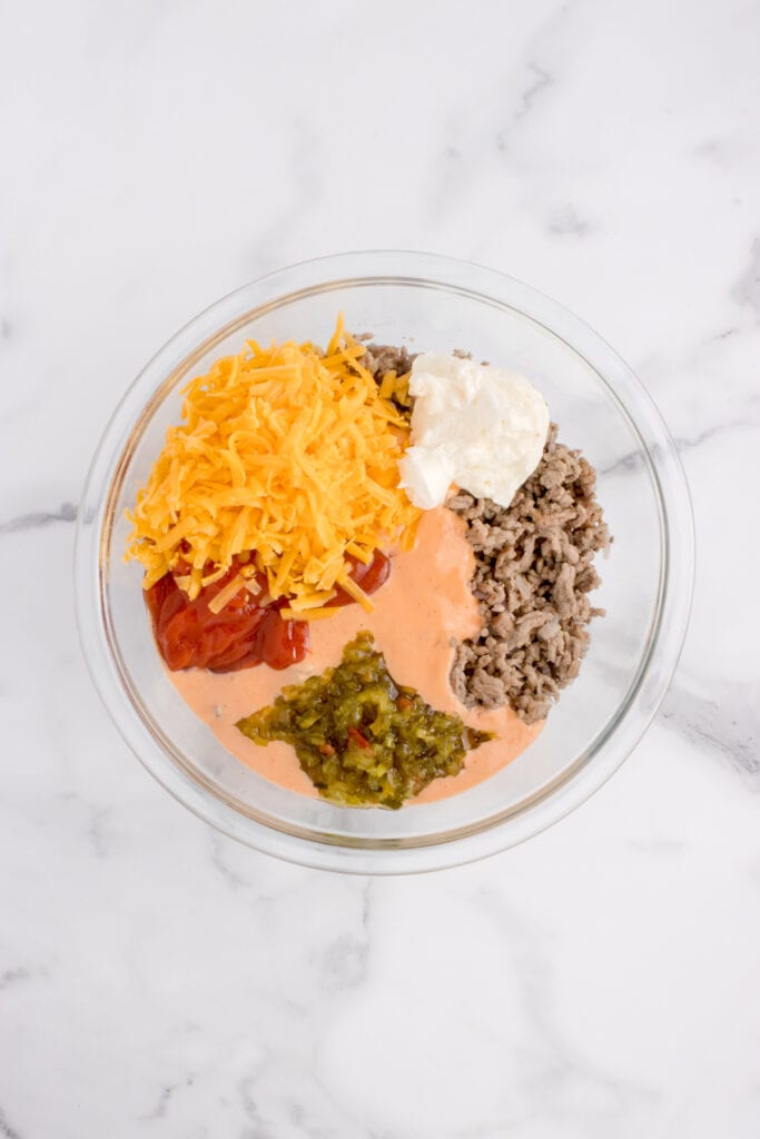 Cooked ground beef with shredded cheddar, mayonnaise, ketchup, Thousand Island dressing, and dill relish in a mixing bowl.