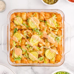 Overhead view of Big Mac Tater Tot Casserole topped with crispy tater tots, dill pickles, shredded lettuce, burger sauce, and sesame seeds.