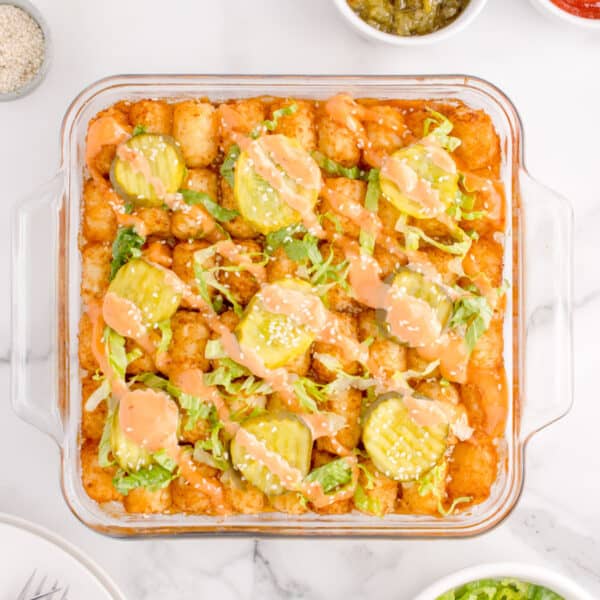 Overhead view of Big Mac Tater Tot Casserole topped with crispy tater tots, dill pickles, shredded lettuce, burger sauce, and sesame seeds.