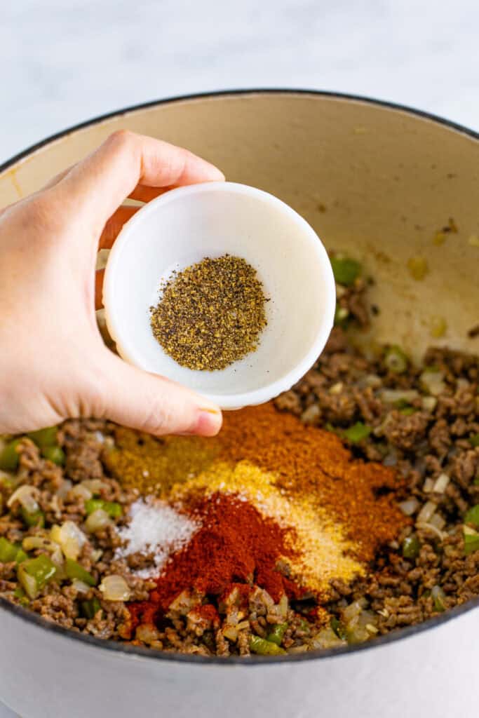 Black pepper being added to the seasoned ground beef mixture in a Dutch oven