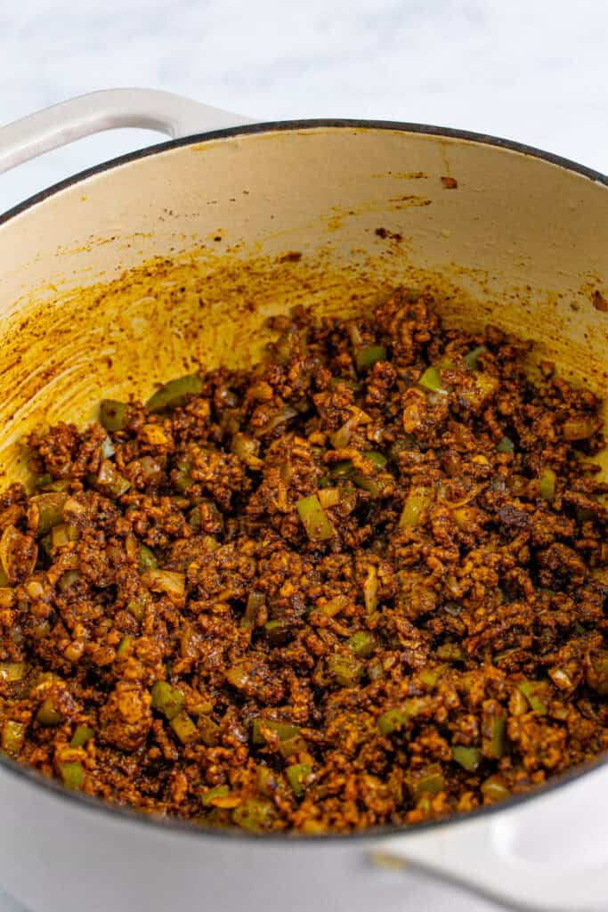 Seasoned ground beef, green bell pepper, and onion mixture cooking in a Dutch oven