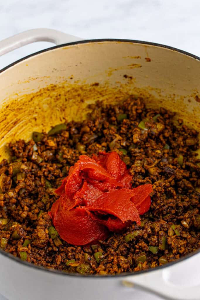 Tomato paste added to seasoned ground beef, peppers, and onions for Chili Mac