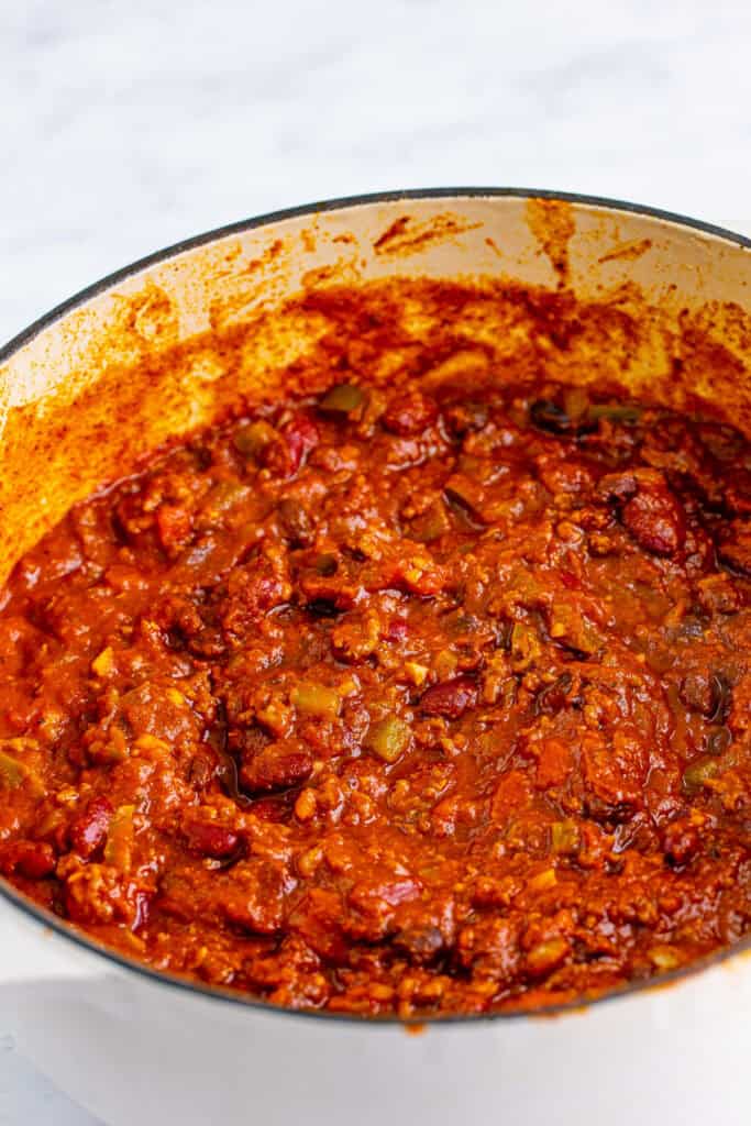 Thick homemade chili with ground beef, beans, tomatoes, peppers, and onions simmering in a Dutch oven