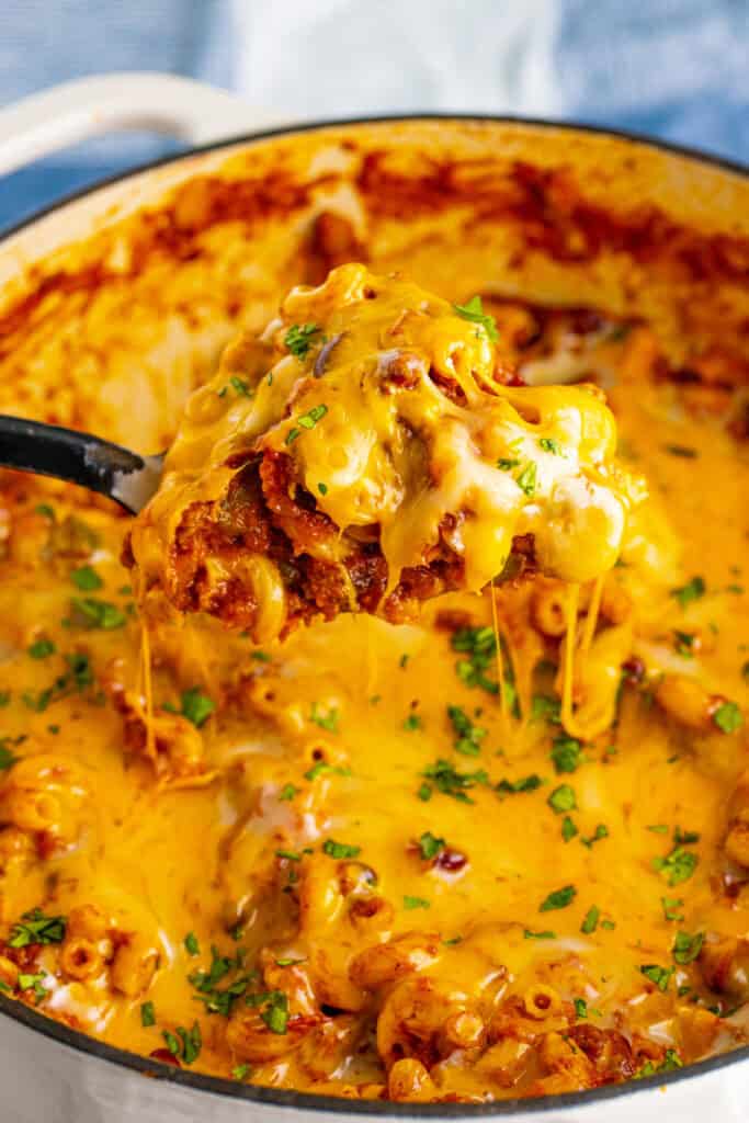 Cheesy Chili Mac lifted from a Dutch oven with melted cheese stretching from the spoon