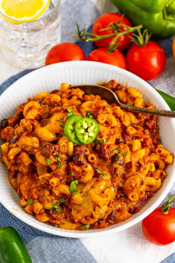 Close-up bowl of homemade Chili Mac topped with melted cheese, jalapeño slices, and fresh herbs
