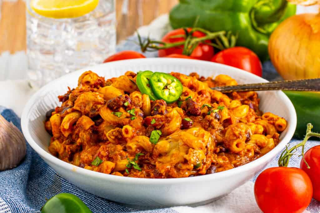 Bowl of homemade Chili Mac with ground beef, beans, macaroni, melted cheese, and jalapeño garnish