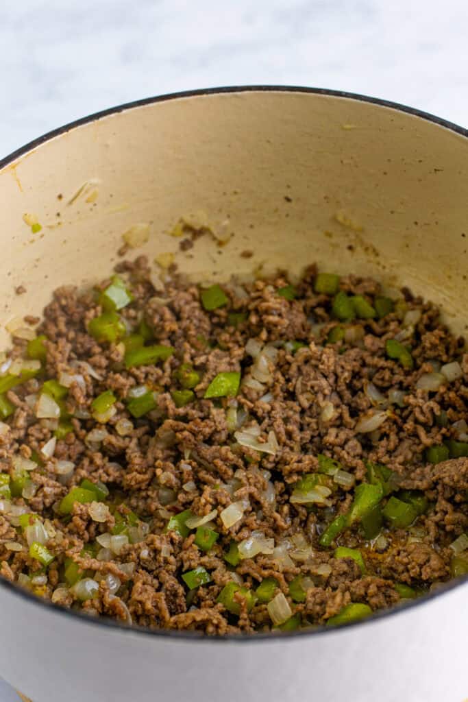 Ground beef cooking with diced green bell pepper and onion in a Dutch oven