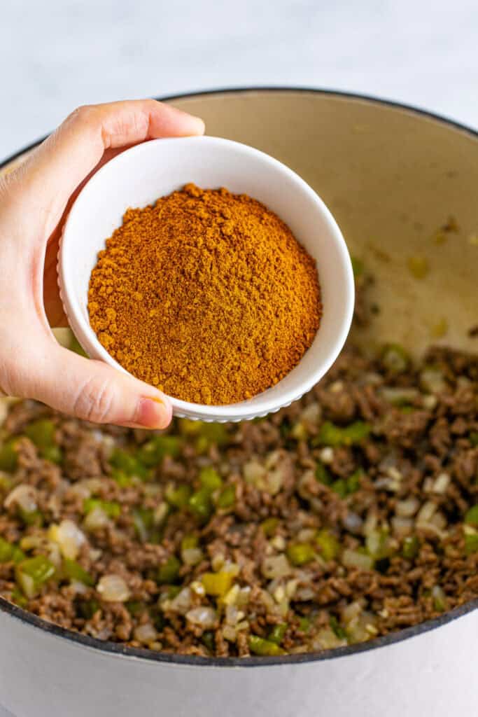 Chili seasoning being added to ground beef, onions, and green bell peppers
