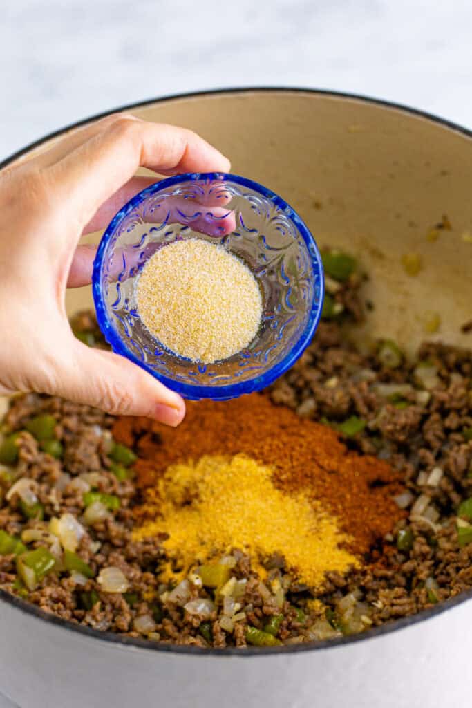 Onion powder being added to the ground beef and seasonings in a Dutch oven