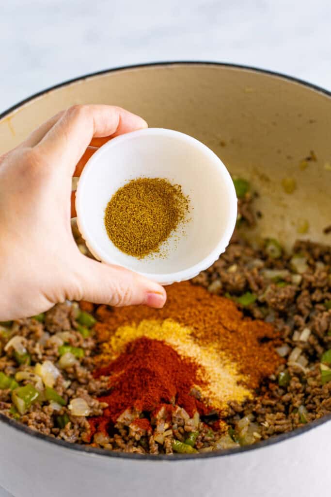 Ground cumin being added to the beef, peppers, onions, and seasonings