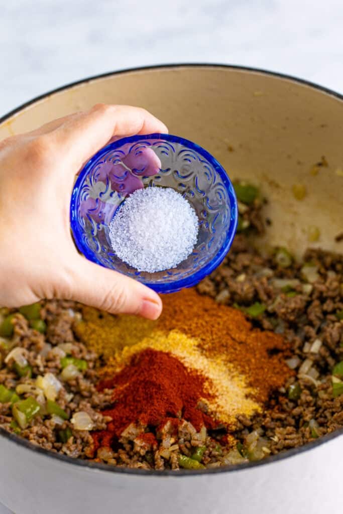 Kosher salt being added to the seasoned ground beef mixture for Chili Mac