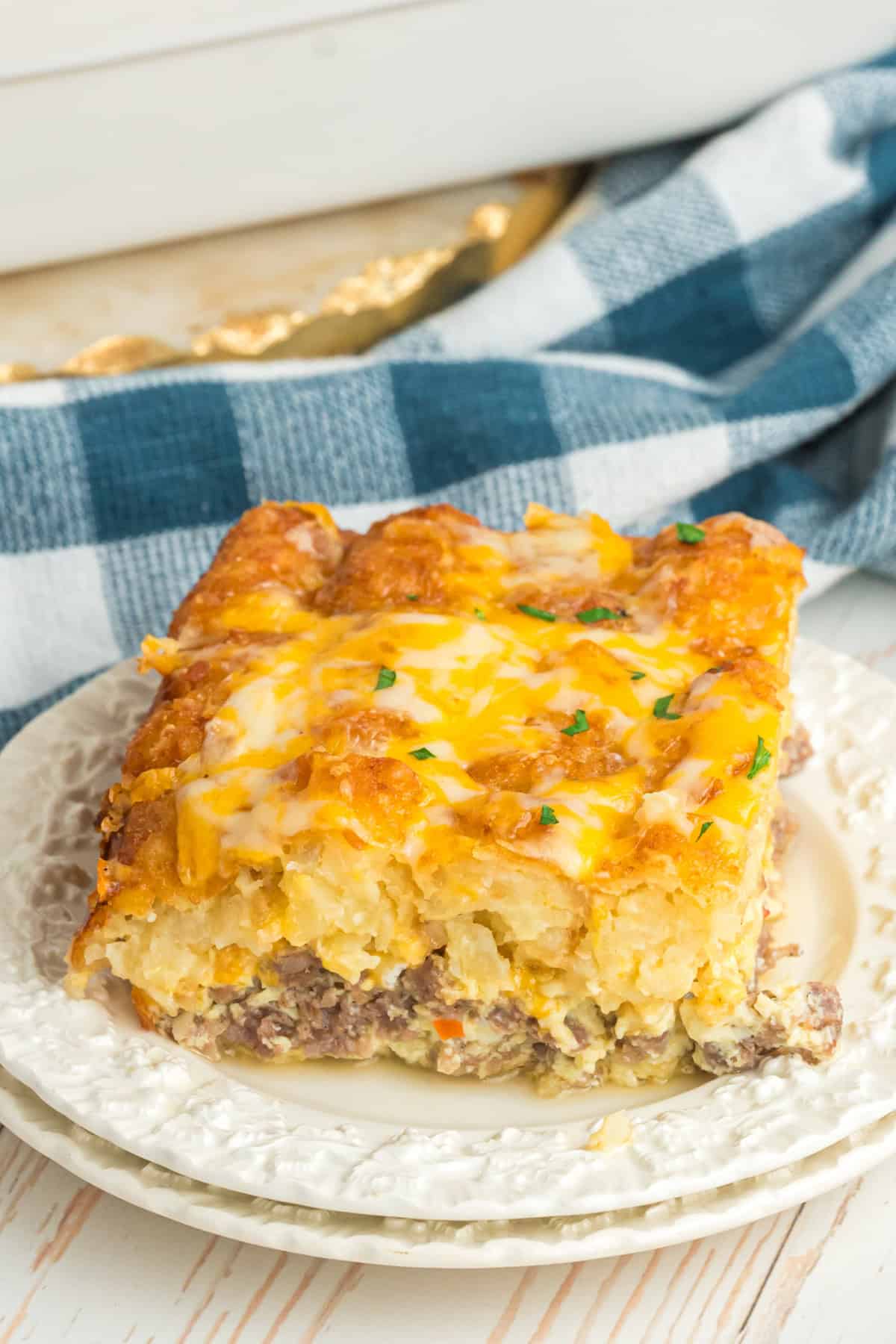 A slice of breakfast tater tot casserole with sausage and eggs on a white plate.