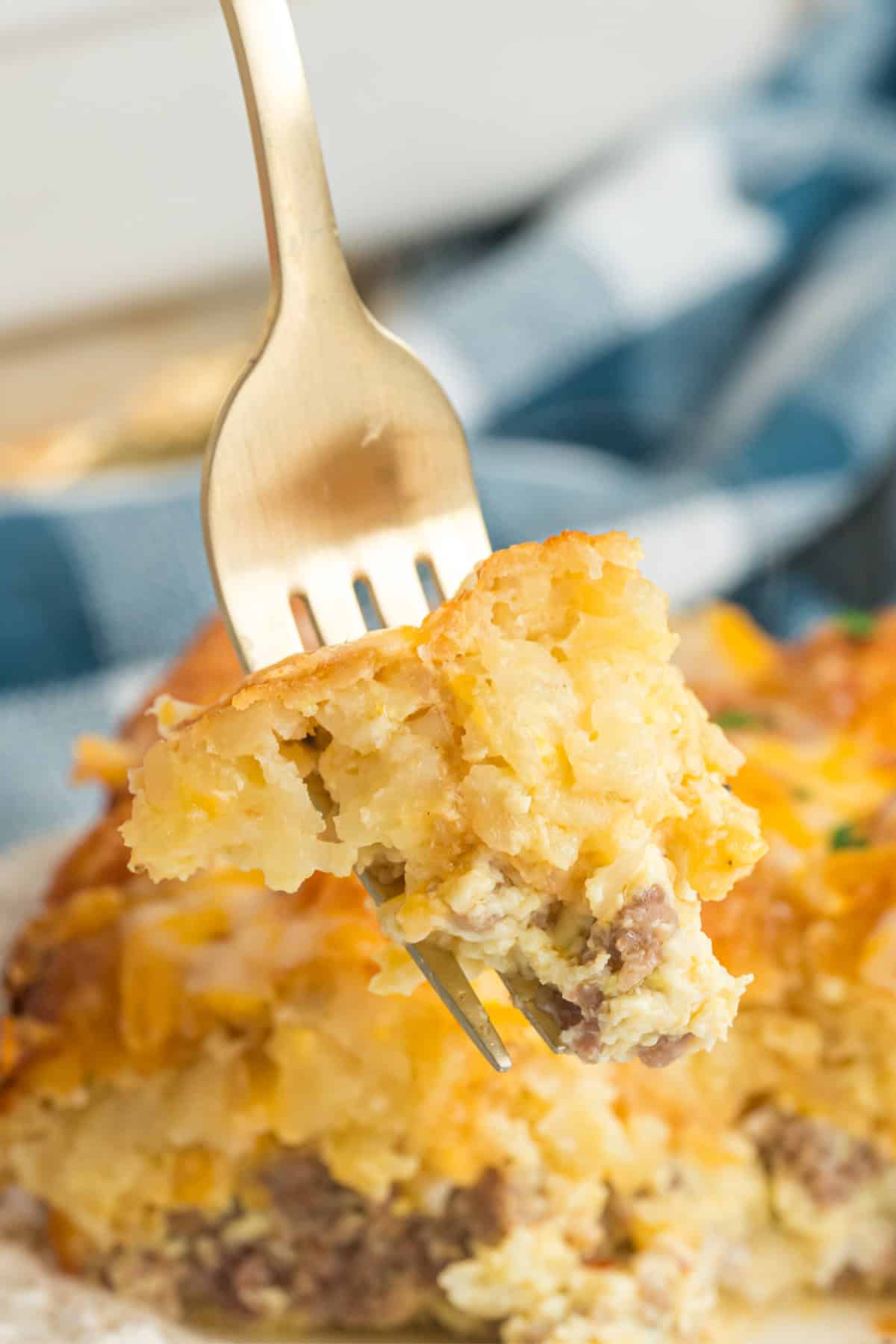 A fork holding a bite of breakfast tater tot casserole with eggs, sausage, and potatoes.