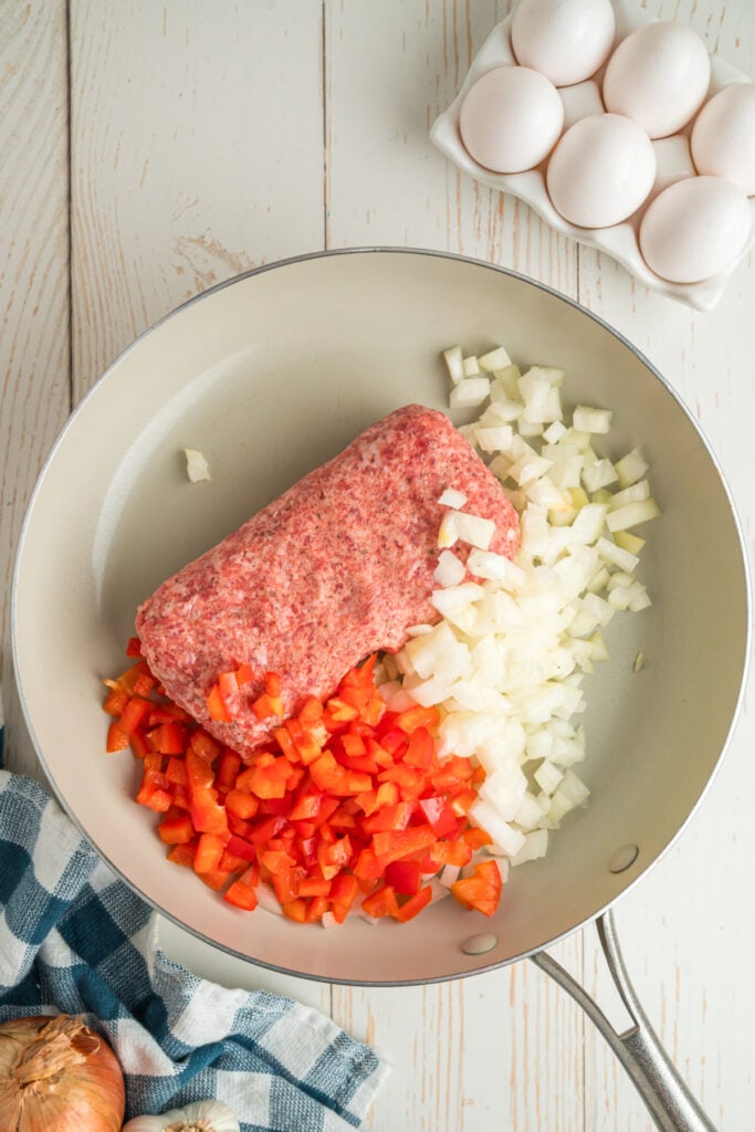 Raw breakfast sausage, diced onion, and red bell pepper in a skillet.