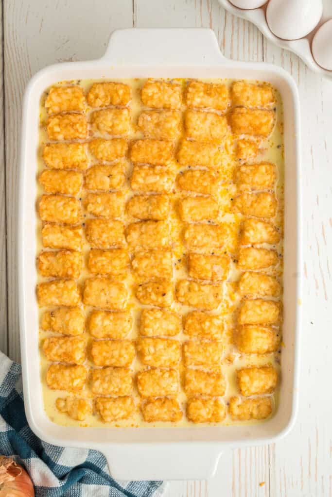 Unbaked breakfast casserole topped with rows of frozen tater tots.